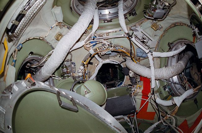 A view of the interior of the docking node of the Russian space station Mir's core module, showing the hatches leading to the station's various modules and the cables and hoses trailing through them.