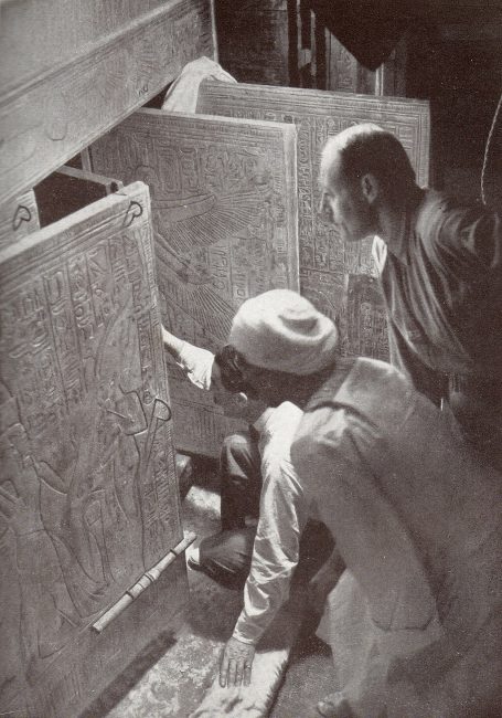Howard Carter (squatting), Arthur Callender and an Egyptian workman, looking into the opened shrines enclosing Tutankhamun's sarcophagus in 1924.